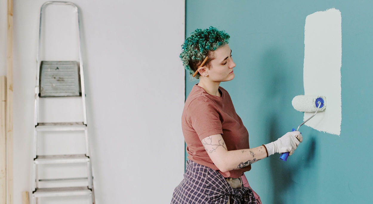 woman painting wall with roller brush during home renovation standing near ladder